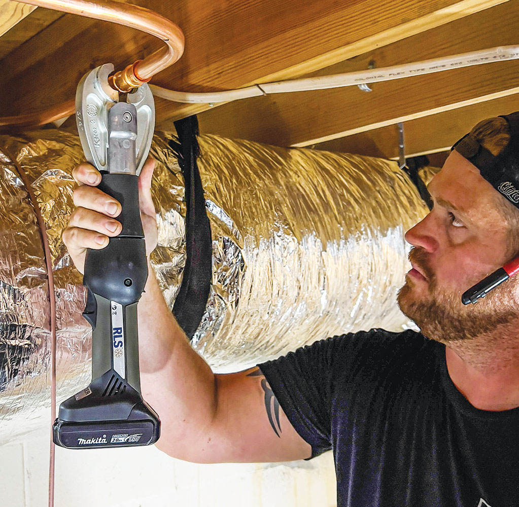 Technician using press fitting tool on mini-split installation in home attic
